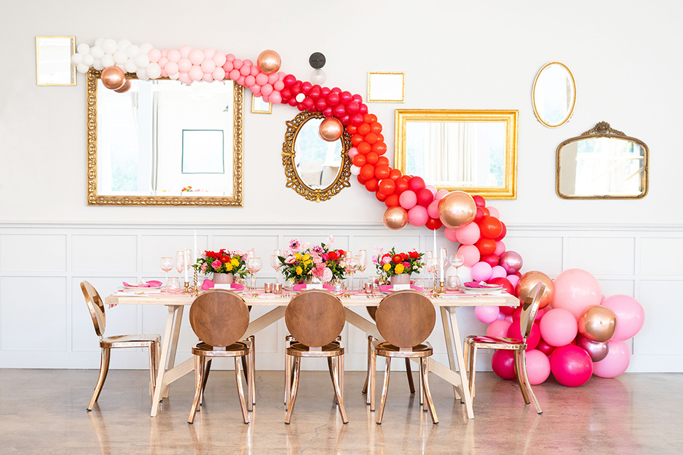 I-love-lucy-shoot-balloons-with-table-set-up-gold-chairs-and-table-with-cascading-pink-balloons-across-the-wall-and-pink-table-decor