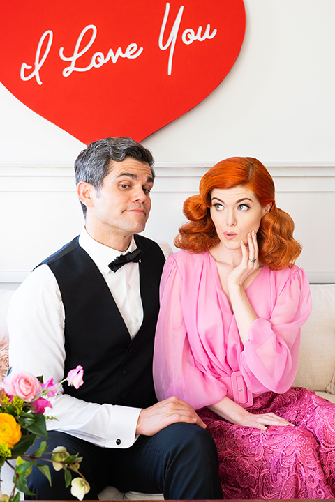 I-love-lucy-shoot-bride-and-groom-by-by-i-love-you-sign-bride-in-a-pink-wide-legged-pant-and-top-with-red-hair-and-red-lipstick-groom-in-a-white-and-black-tuxedo