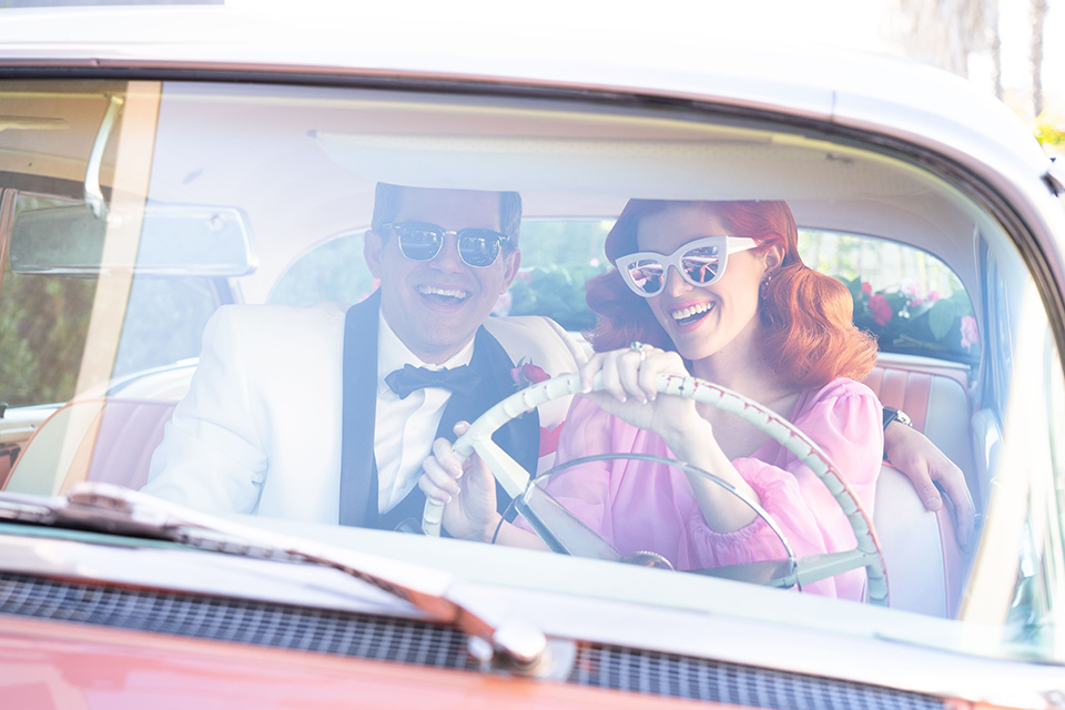 I-love-lucy-shoot-bride-and-groom-in-car-bride-in-a-pink-wide-legged-pant-and-top-with-red-hair-and-red-lipstick-groom-in-a-white-and-black-tuxedo