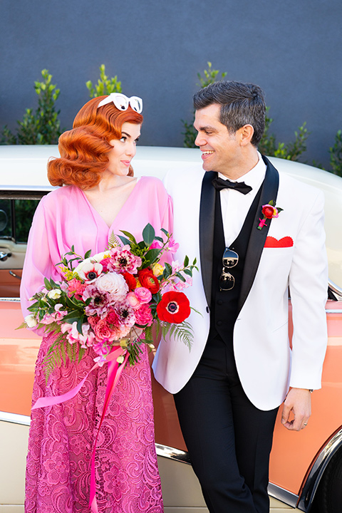 I-love-lucy-shoot-bride-and-groom-standing-by-car-bride-in-a-pink-wide-legged-pant-and-top-with-red-hair-and-red-lipstick-groom-in-a-white-and-black-tuxedo