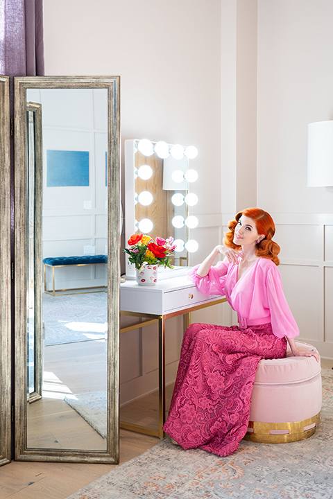 I-love-lucy-shoot-bride-sitting-at-vanity-bride-in-a-pink-wide-legged-pant-and-top-with-red-hair-and-red-lipstick-groom-in-a-white-and-black-tuxedo