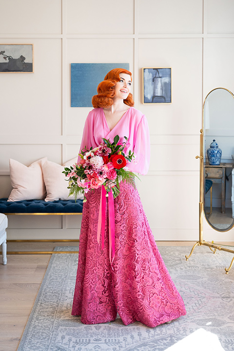 I-love-lucy-shoot-bride-standing-with-flowers-bride-in-a-pink-wide-legged-pant-and-top-with-red-hair-and-red-lipstick-groom-in-a-white-and-black-tuxedo