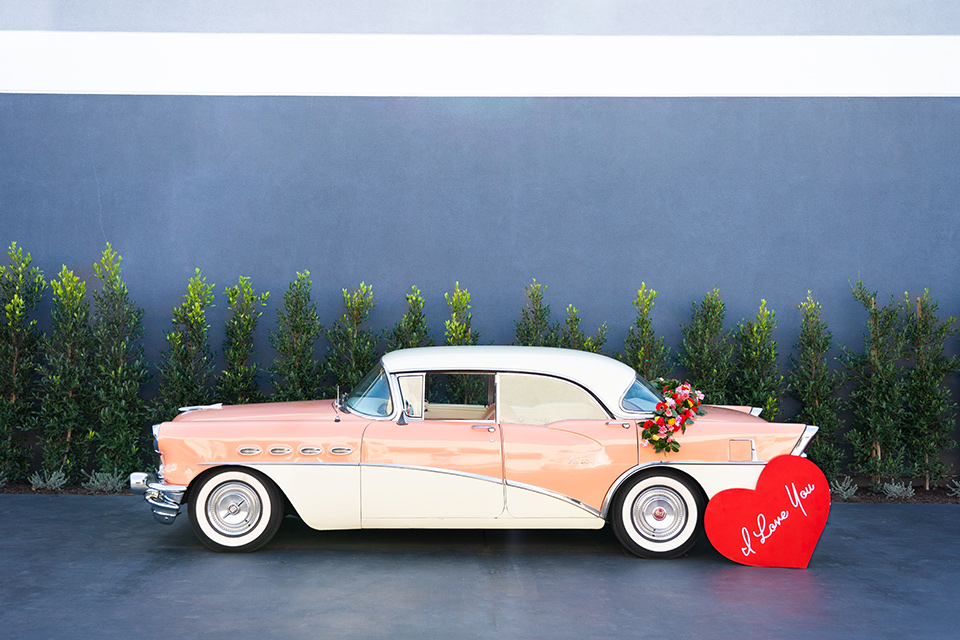 I-love-lucy-shoot-car-bride-in-a-pink-wide-legged-pant-and-top-with-red-hair-and-red-lipstick-groom-in-a-white-and-black-tuxedo