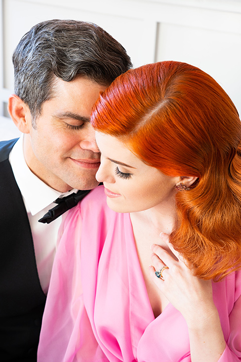 I-love-lucy-shoot-close-up-on-bride-and-groom-bride-in-a-pink-wide-legged-pant-and-top-with-red-hair-and-red-lipstick-groom-in-a-white-and-black-tuxedo