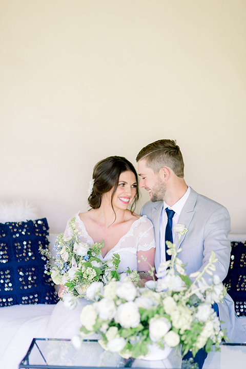bride and groom on the couch outside, bride in a flowing gown with a lace bodice and cap sleeves, the groom in a light grey suit coat with dark blue pants and a long tie