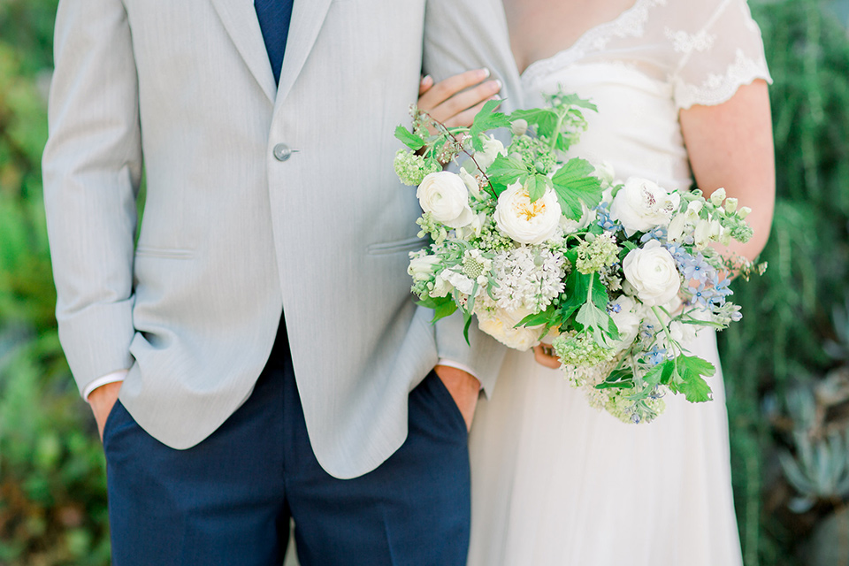 bride in a flowing gown with a lace bodice and cap sleeves, the groom in a light grey suit coat with dark blue pants and a long tie 