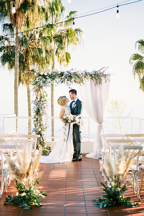 The-Inn-at-Laguna-Beach-bride-and-groom-at-ceremony-bride-in-a-silk-dress-with-a-boat-neckline-and-hair-up-in-a-bun-and-groom-in-a-slate-blue-suit-with-a-matching-bow-tie