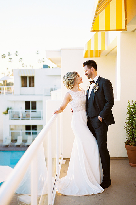 The-Inn-at-Laguna-Beach-bride-and-groom-on-the-balcony-bride-in-a-silk-dress-with-a-boat-neckline-and-hair-up-in-a-bun-and-groom-in-a-slate-blue-suit-with-a-matching-bow-tie