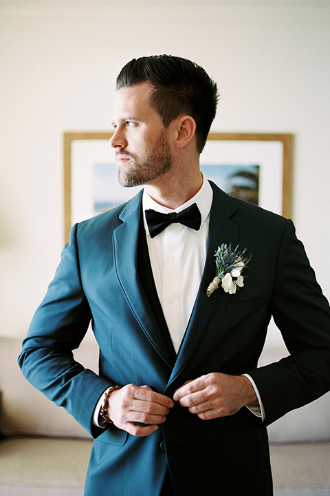 The-Inn-at-Laguna-Beach-groom-buttonging-his-jacket-groom-in-a-grey-blue-suit-with-a-matching-bow-tie