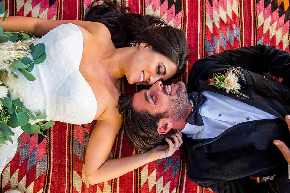 Intercontinental-elopement-shoot-bride-and-groom-on-blanket-groom-in-velvet-tuxedo-with-black-ants-and-a-black-bow-tie-bride-in-a-flowing-gown-with-straps-and-lace