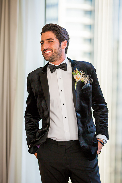 Intercontinental-elopement-shoot-groom-in-black-velvet-by-windows-in-a-velvet-black-tuxedo-and-black-bow-tie