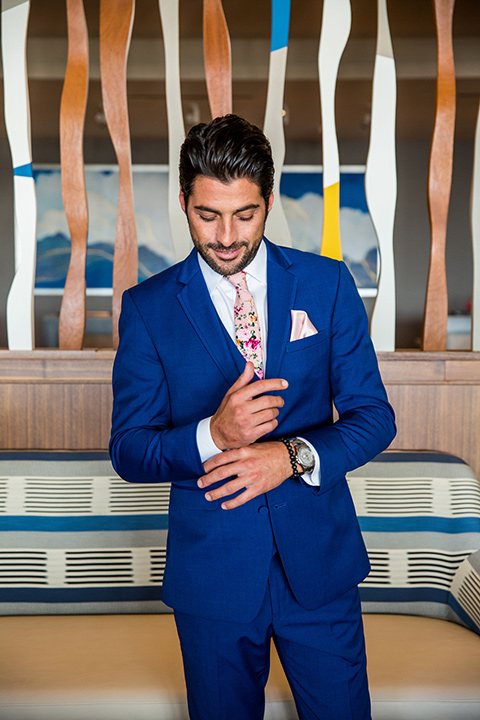 Intercontinental-elopement-shoot-groom-in-blue-fixing-cuff-of=cobalt-blue-suit-with-a-pink-floral-long-tie