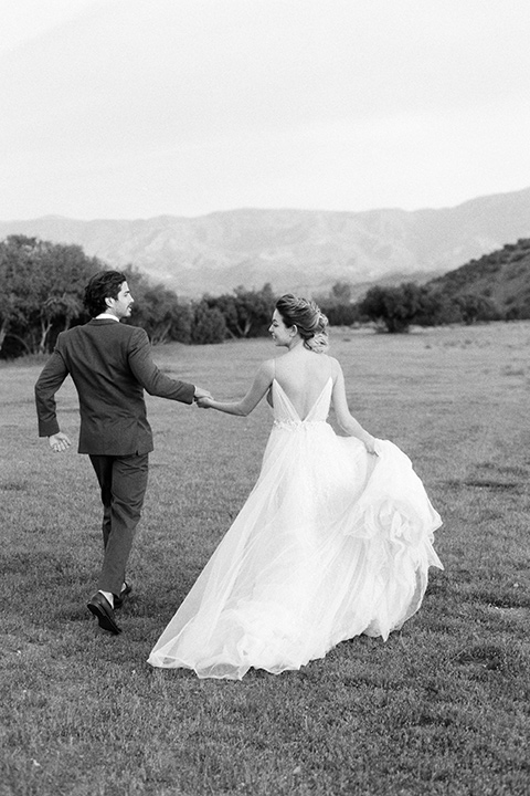 italian-style-wedding-bride-and-groom-black-ad-white-photo-of-them-walking-away-bride-in-a-flowing-gown-with-straps-and-her-hair-up-groom-in-a-grey-tuxedo