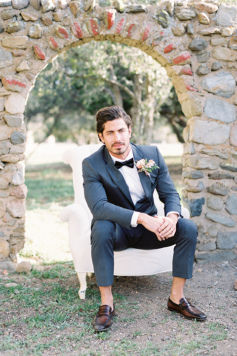 italian-style-wedding-groom-sitting-on-chair-in-a-grey-tuxedo-with-black-bow-tie