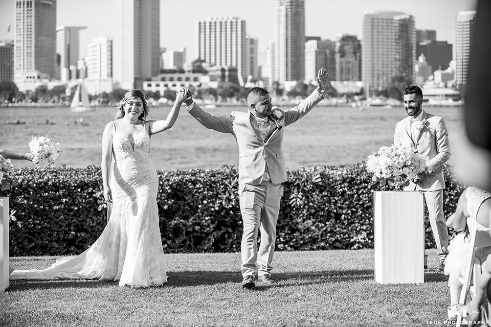 Wedding bride and groom after ceremony with the bride wearing an ivory lace gown with thin straps and the groom in a tan suit with a pink bow tie