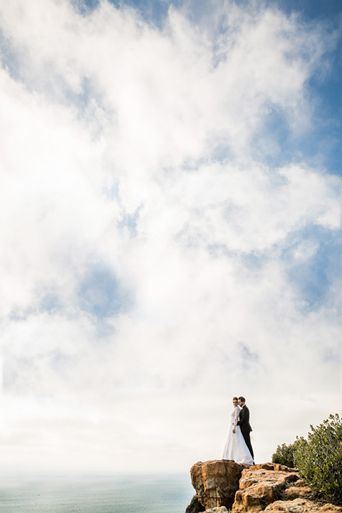  bride and groom on a cliff in San Diego with the bride in a lace and tulle gown with long sleeves and high neckline groom in a black tuxedo with black bow tie