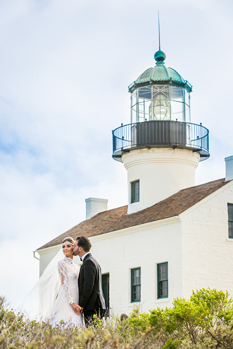 San Diego bride and groom by the lighthouse with the bride in a lace and tulle gown with long sleeves and high neckline groom in a traditional black tuxedo with black bow tie