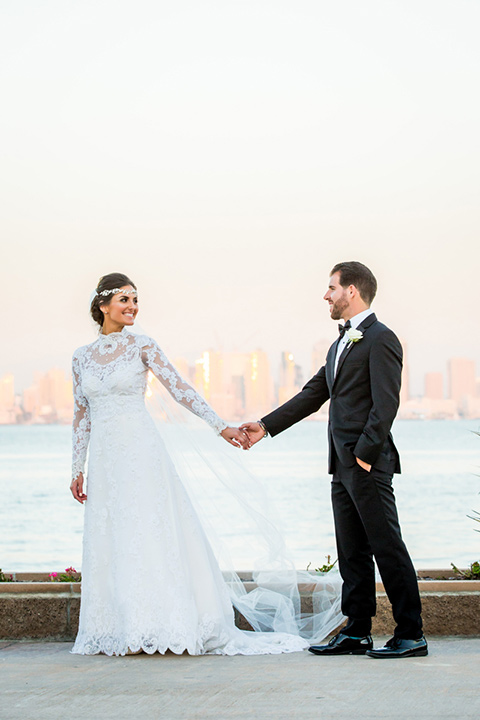 Admiral Kidd Club bride and groom walking bride in a lace and tulle gown with long sleeves and high neckline groom in a black tuxedo with black bow tie