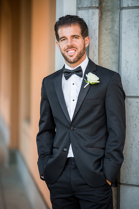 wedding groom in a black tuxedo posing in front of Admiral Kidd Club