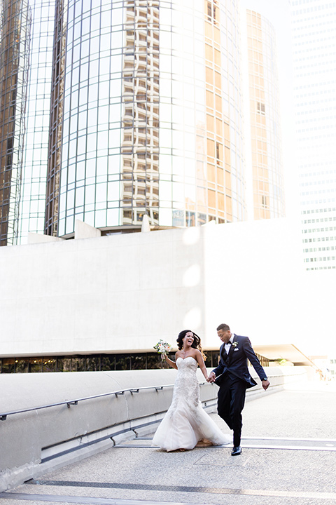 walt-disney-concert-hall-bride-and-groom-running-bride-in-a-mermaid-style-gown-with-a-elbow-length-veil-groom-in-a-navy-shawl-lapel-tuxedo