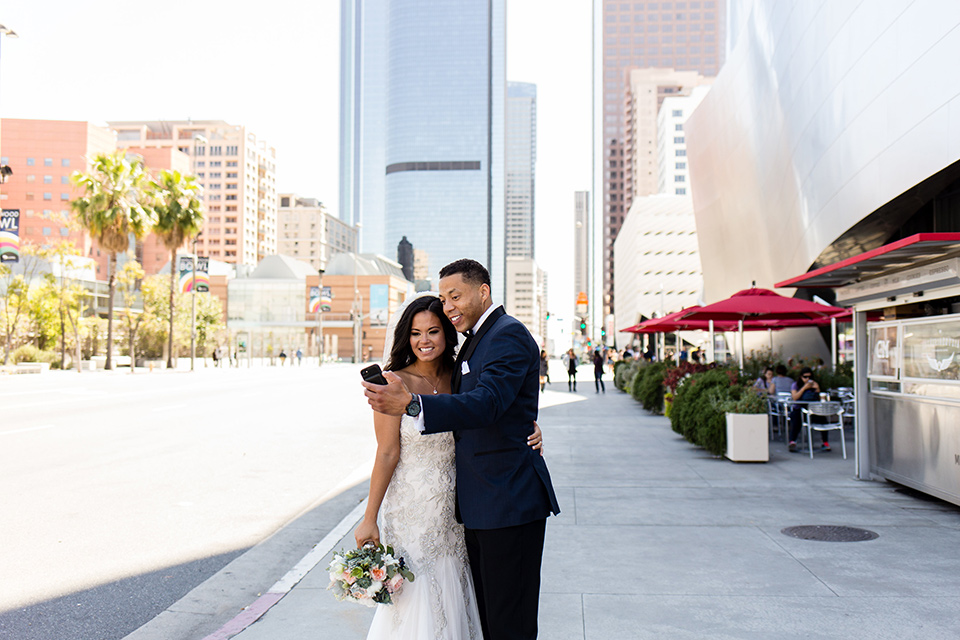 walt-disney-concert-hall-bride-and-groom-taking-a-selfie-bride-in-a-strapless-white-gown-with-a-sweetheart-neckline-groom-in-a-navy-tuxedo