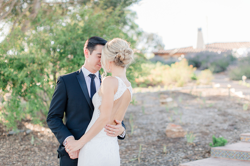 Arroyo-Grande-Wedding-bride-and-groom-standing-close-together-on-steps-bride-in-a-boho-style-gown-with-a-keyhole-back-and-high-neckline-and-fringe-white-the-groom-wore-a-traditional-black-tuxedo-and-black-long-tie