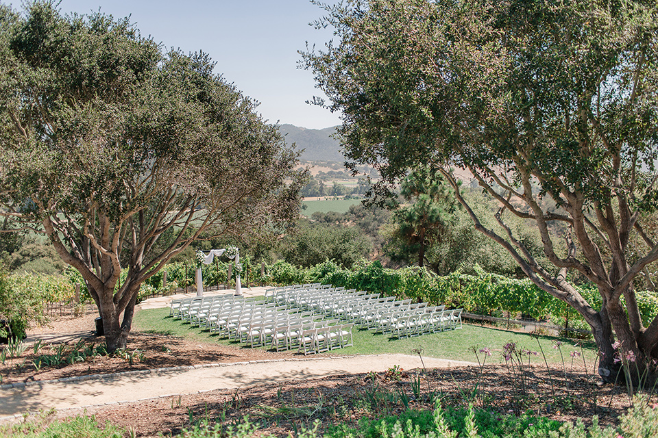 Arroyo-Grande-Wedding-ceremony-space-in-a-grass-area-with-simple-wooden-chairs-and-archway-surrounded-by-trees