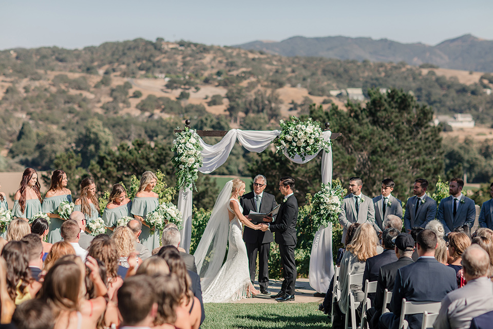 Arroyo-Grande-Wedding-ceremony-bride-in-a-boho-style-gown-with-a-keyhole-back-and-high-neckline-and-fringe-white-the-groom-wore-a-traditional-black-tuxedo-and-black-long-tie