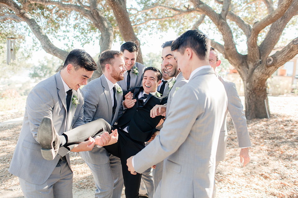 Arroyo-Grande-Wedding-groom-being-held-up-by-groomsmen-the-groom-wore-a-traditional-black-tuxedo-and-black-long-tie-while-the-groomsmen-wore-light-grey-suits-with-black-ties