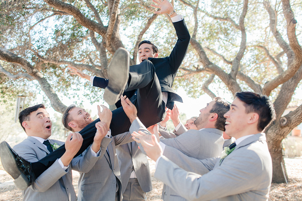 Arroyo-Grande-Wedding-groom-being-thrown-by-groomsmen-the-groom-wore-a-traditional-black-tuxedo-and-black-long-tie-while-the-groomsmen-wore-light-grey-suits-with-black-ties