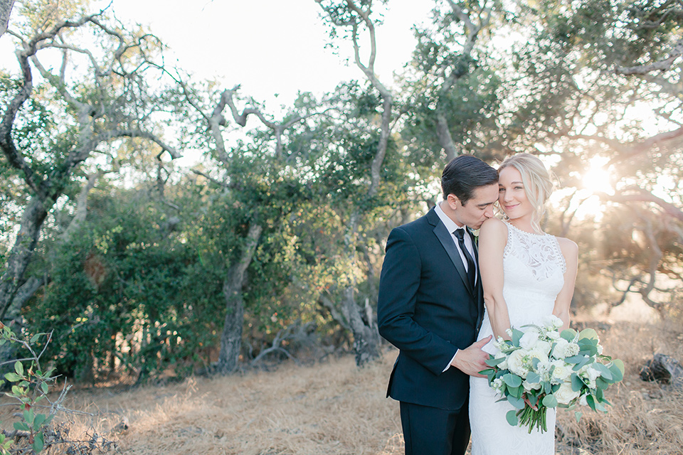 Arroyo-Grande-Wedding-groom-kissing-brides-shoulder-bride-in-a-boho-style-gown-with-a-keyhole-back-and-high-neckline-and-fringe-white-the-groom-wore-a-traditional-black-tuxedo-and-black-long-tie