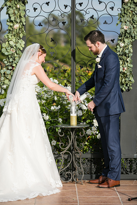 bride and groom pouring champagne at wedding venue in front of green vines and white florals