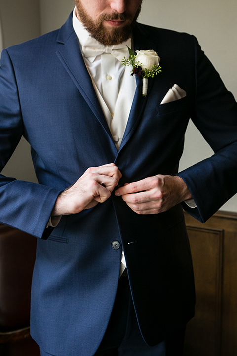 groom buttons button on blue suit with white bow tie, white pocket square, and white floral 