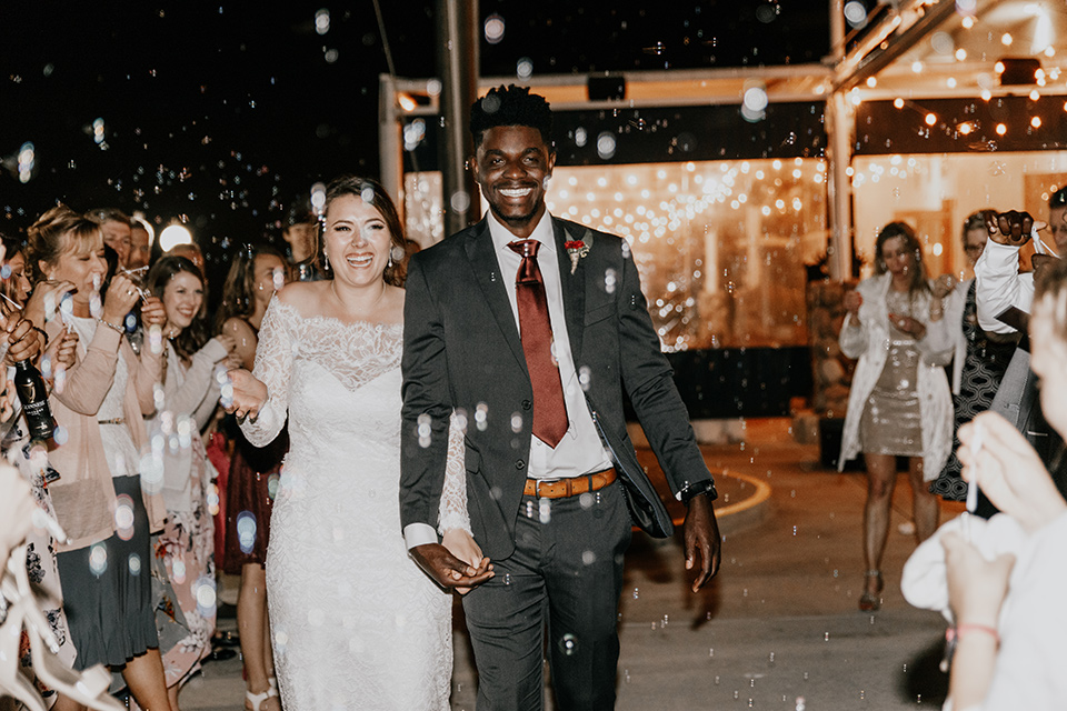 coronado-yacht-club-wedding-bride-and-groom-leaving-weddings-bride-in-a-lace-form-fitting-gown-with-sleeves-groom-in-a-charcoal-grey-suit-with-red-tie