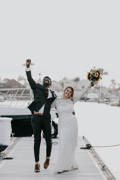 coronado-yacht-club-wedding-bride-and-groom-with-fists-in-the-air-bride-in-a-lace-dress-with-sleeves-and-groom-in-a-charcoal-suit-with-a-red-tie