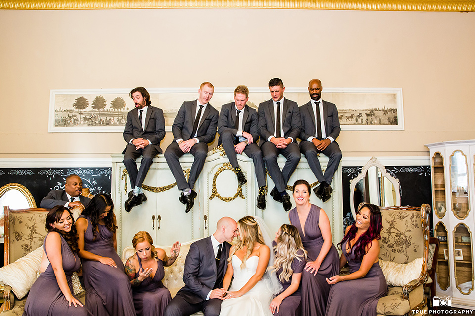 twin-oaks-weddings-bridal-party-sitting-bridesmaids-in-long-purple-dresses-with-different-necklines-groomsmen-in-grey-suits-bride-in-a-strapless-fit-and-flare-gown-with-a-sweetheart-neckline-groom-in-a-charcoal-grey-suit-with-black-long-tie