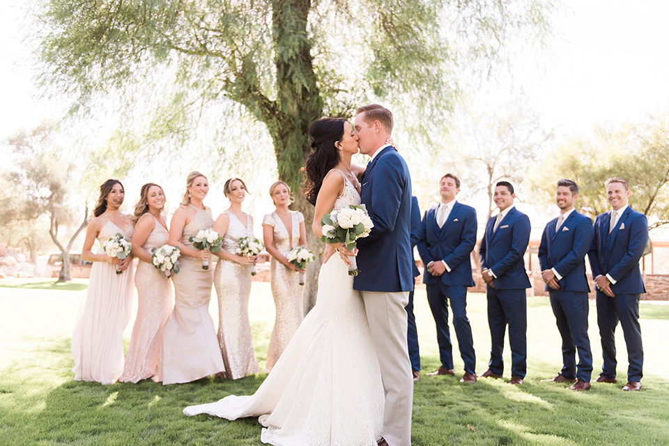 tanque-verde-ranch-arizona-wedding-brialparty-bridesmaids-in-blush-toned-dresses-and-groomsmen-in-dark-blue-suits-the-bride-in-a-white-formfitting-gown-with-thin-straps-and-the-groom-and-in-grey-suit-pants-and-a-blue-suit-coat