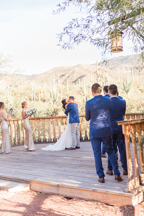 tanque-verde-ranch-arizona-wedding-bride-and-groom-first-kiss-the-bride-in-a-white-formfitting-gown-with-thin-straps-and-the-groom-in-grey-pants-and-a-blue-suit-coat