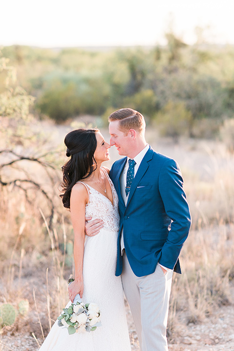 tanque-verde-ranch-arizona-wedding-bride-and-groom-looking-out-at-desert-the-bride-in-a-white-formfitting-gown-with-thin-straps-and-the-groom-in-grey-suit-pants-and-a-navy-blue-suit-coat