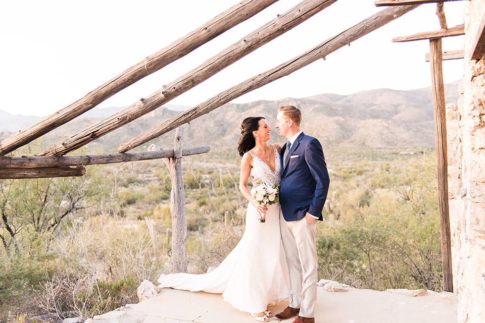 tanque-verde-ranch-arizona-wedding-bride-and-groom-ouside-venue-the-bride-in-a-white-formfitting-gown-with-thin-straps-and-the-groom-and-in-grey-suit-pants-and-a-blue-suit-coat