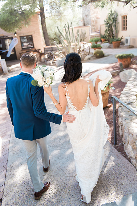 tanque-verde-ranch-arizona-wedding-bride-and-groom-walking-away-bride-in-a-white-formfitting-gown-with-thin-straps-and-the-groom-in-grey-pants-and-a-blue-suit-coat