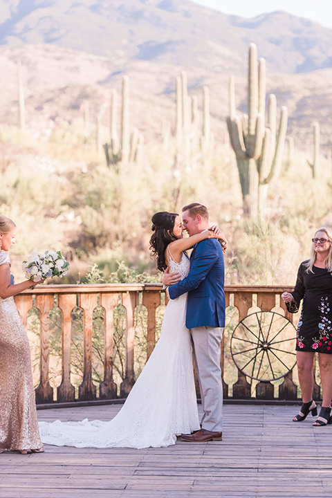 tanque-verde-ranch-arizona-wedding-first-kiss-the-bride-in-a-white-formfitting-gown-with-thin-straps-and-the-groom-in-grey-suit-pants-and-a-navy-blue-suit-coat