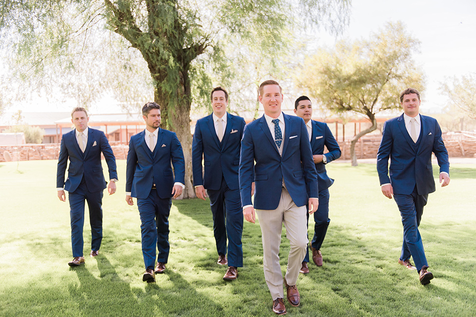 tanque-verde-ranch-arizona-wedding-groom-and-groomsmen-walking-groomsmen-in-dark-blue-suits-the-groom-and-in-grey-suit-pants-and-a-blue-suit-coat