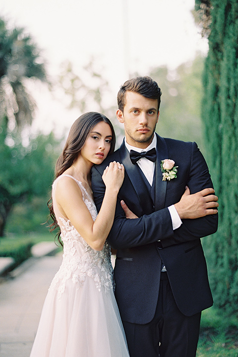 Kimberly-crest-house-shoot-bride-and-groom-looking-at-camera-groom-in-a-black-tuxedo-with-white-shirt-and-black-bow-tie-bride-in-a-flowing-white-gown-with-a-full-skirt