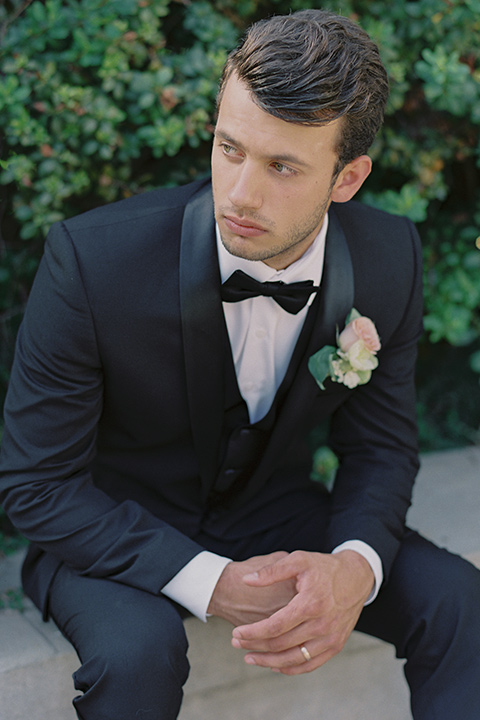 Kimberly-crest-house-shoot-groom-sitting-in-a-black-tuxedo-with-white-shirt-and-black-bow-tie