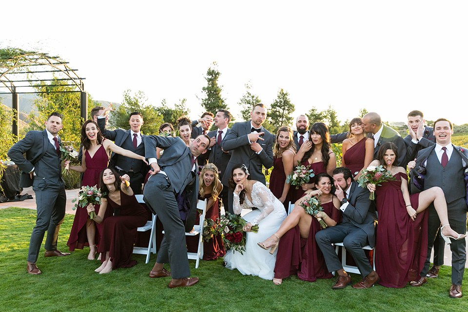  bride in a white lace gown with a full skirt and long lace sleeves and her hair in a finger wave and the groom in a charcoal tuxedo with a black bow tie and the groomsmen in charcoal tuxedo and bridesmaids in burgundy gowns