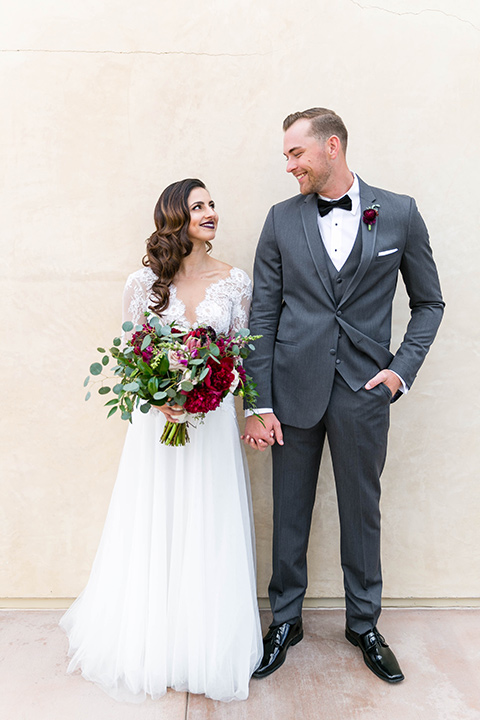 bride in a white lace gown with a full skirt and long lace sleeves and her hair in a finger wave and the groom in a charcoal tuxedo with a black bow tie
