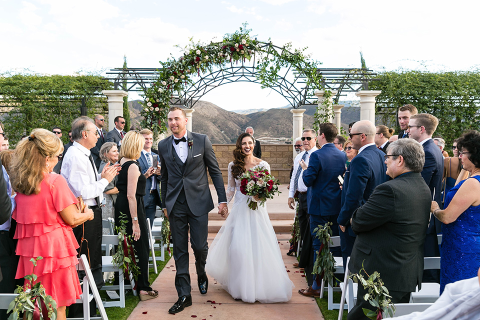  bride in a white lace gown with a full skirt and long lace sleeves and her hair in a finger wave and the groom in a charcoal tuxedo