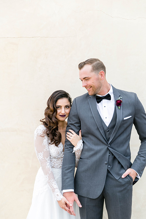  bride in a white lace gown with a full skirt and long lace sleeves and her hair in a finger wave and the groom in a charcoal tuxedo with a black bow tie 