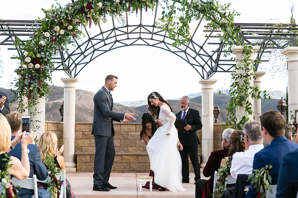  bride in a white lace gown with a full skirt and long lace sleeves and her hair in a finger wave and the groom in a charcoal tuxedo